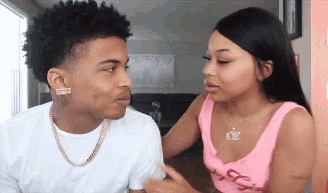 a man and a woman are looking at each other and the woman is wearing a necklace with the letter k on it