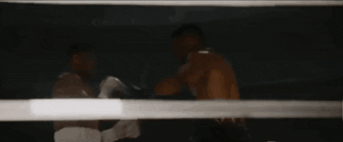 two men are fighting in a boxing ring in a dark room
