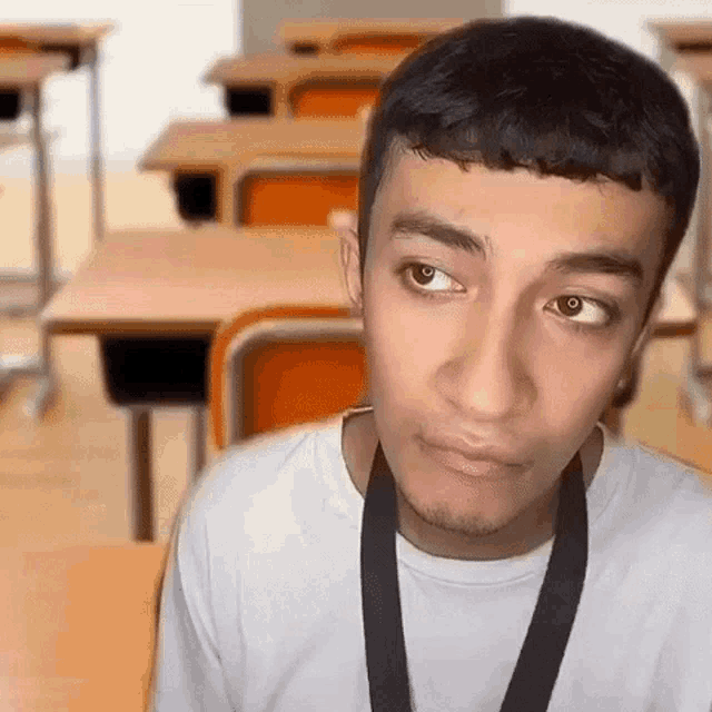 a young man is sitting at a desk in a classroom wearing a lanyard .