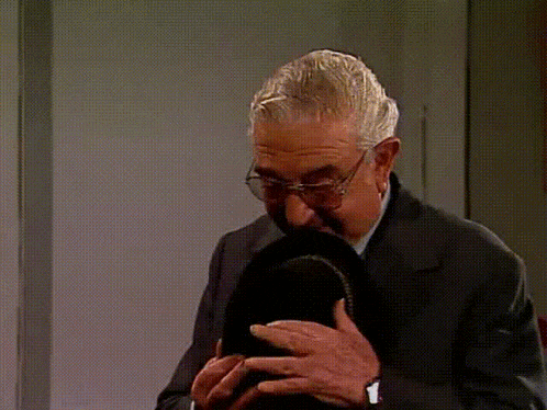 a man wearing glasses and a suit holds a black hat