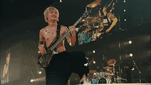 a shirtless man is playing a bass guitar on a stage with a large screen behind him that says " one "
