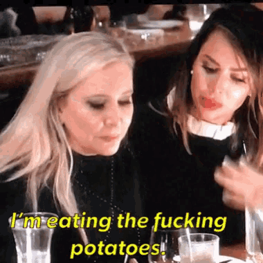 two women are sitting at a table and one of them says i 'm eating the fucking potatoes .