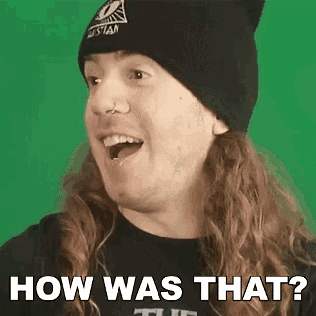 a man with long hair is wearing a black beanie and a black shirt that says how was that ?