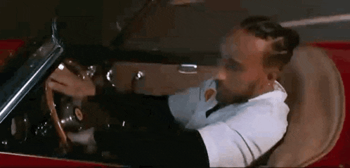 a man is driving a red convertible car down a road .