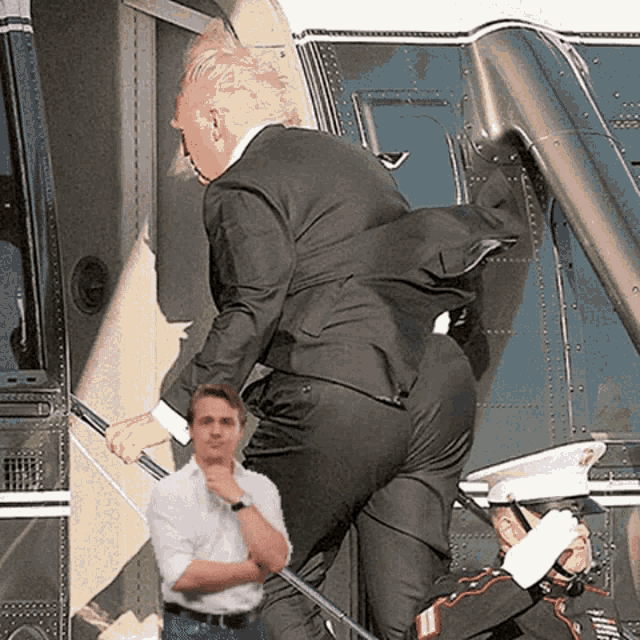 a man in a suit is getting out of a helicopter while a man in a white shirt looks on