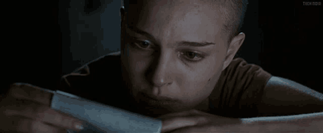 a woman with a shaved head is looking at a piece of paper with the word teen on it