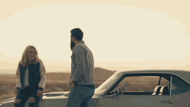 a man and a woman sitting on the side of a car