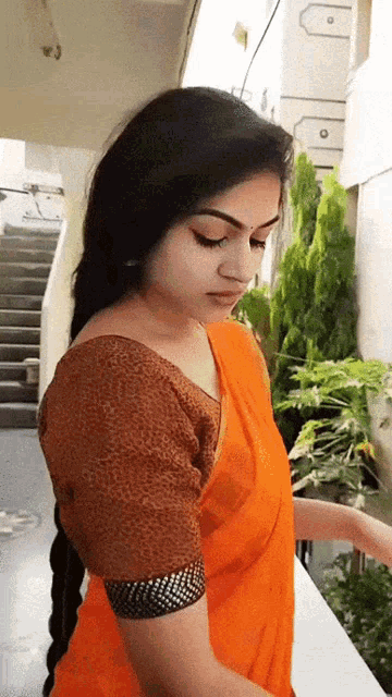 a woman wearing an orange saree and a brown blouse is standing on a balcony