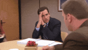 a man in a suit and tie is sitting at a table with another man