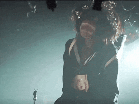 a girl in a school uniform is standing in front of a microphone in the dark .