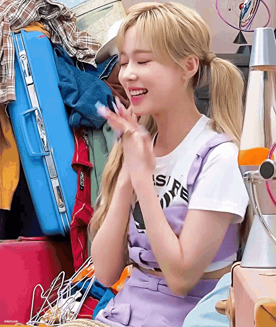 a woman wearing a white t-shirt that says ' desire ' on it smiles in front of a pile of luggage