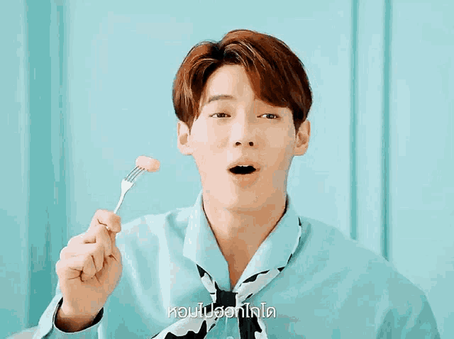 a man in a blue shirt is holding a fork in front of his nose