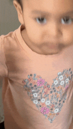 a close up of a baby wearing a pink shirt with a heart on it
