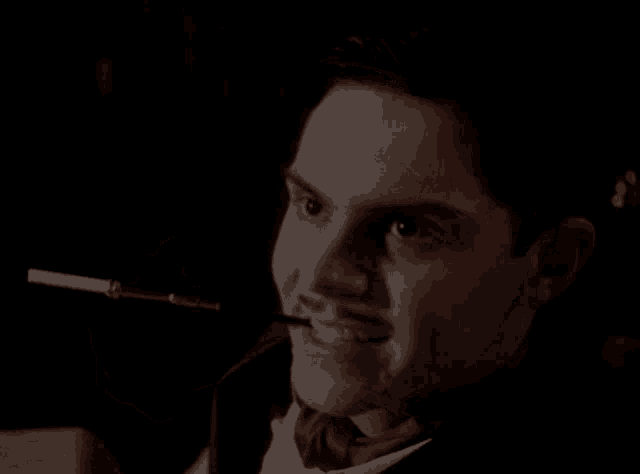 a man in a tuxedo is smoking a cigarette and wearing a ring on his finger