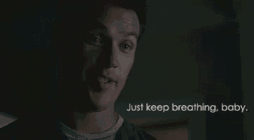 a man in a dark room with the words `` just keep breathing , baby '' behind him .