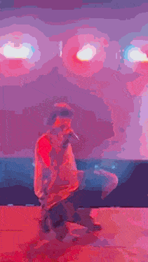 a man in a red shirt is kneeling down and singing into a microphone