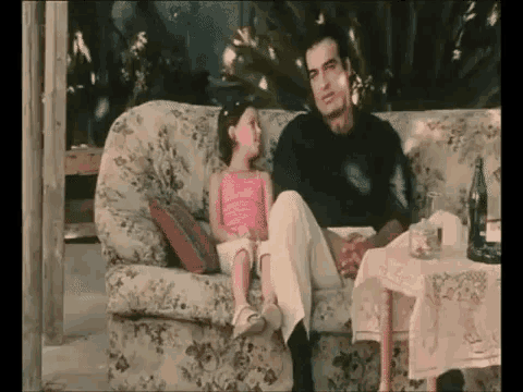a little girl is sitting on a couch next to a man .