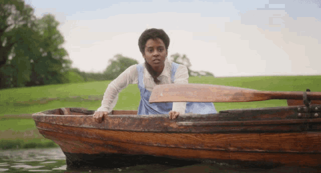 a woman in a blue dress is sitting in a wooden boat