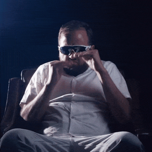a man wearing sunglasses is sitting in a dark room