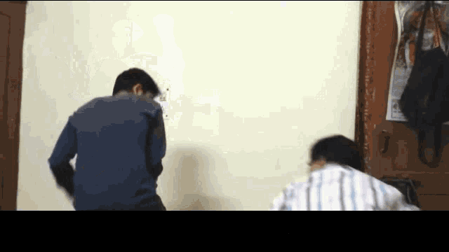 a man in a blue shirt is standing in front of a wall