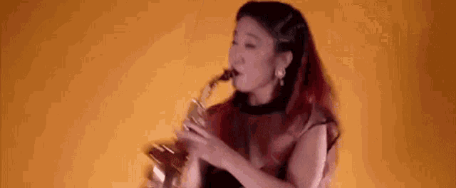 a woman with red hair is playing a saxophone in front of a yellow background .