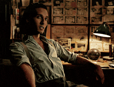 a man wearing suspenders sits in front of a wall that has pictures on it