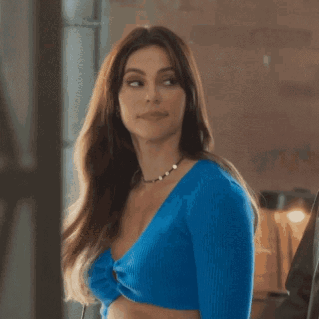 a woman wearing a blue sweater and a necklace is looking at the camera
