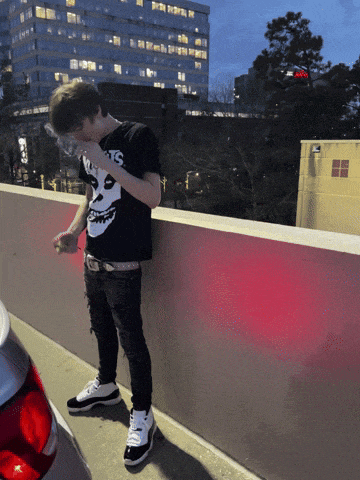 a man wearing a t-shirt that says misfits is standing next to a car