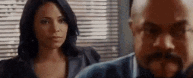 a man and a woman are standing next to each other in front of a window with blinds .