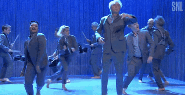 a man in a suit stands on a stage with a snl logo in the corner