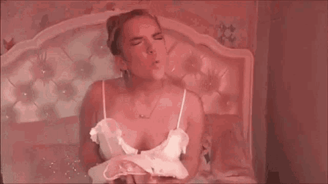 a woman is blowing a kiss while sitting on a bed in a pink room .
