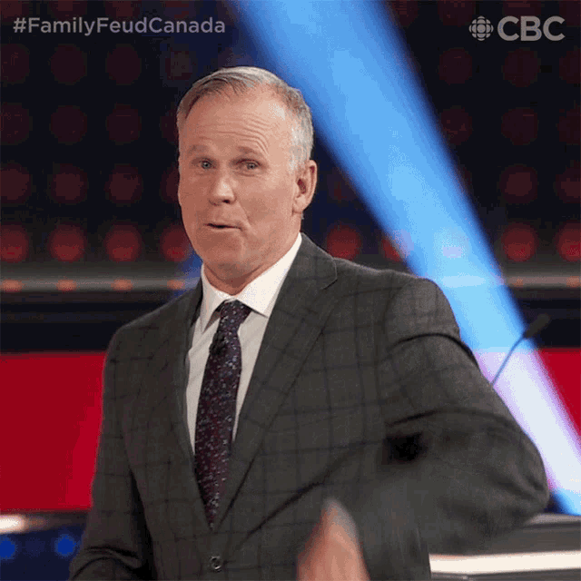 a man in a suit and tie is standing in front of a microphone with the words family feud canada on the bottom