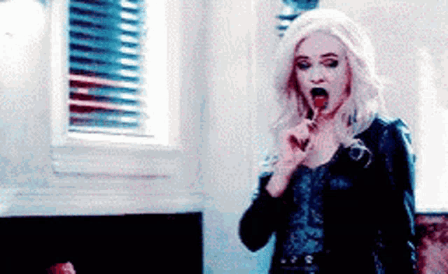 a woman in a wig is licking a lollipop in a room .