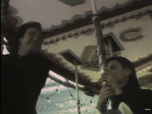 a man and a woman are standing in front of a carousel with the letter c on it