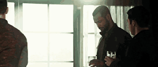 three men are standing in front of a window and one of them is holding a glass of whiskey