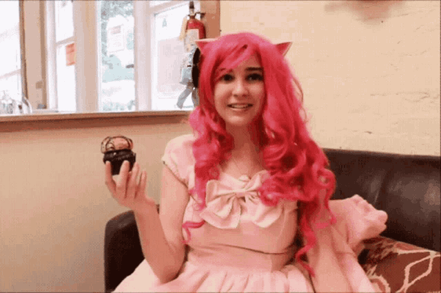 a woman with pink hair is holding a small cupcake