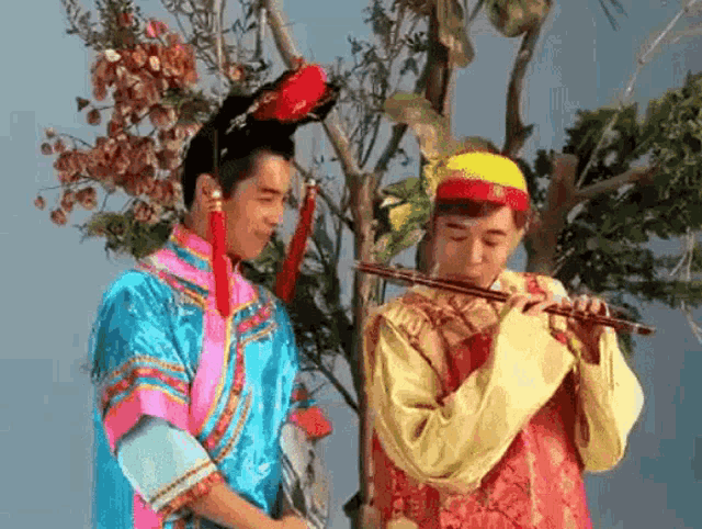 a man in a costume is playing a flute next to another man in a costume .