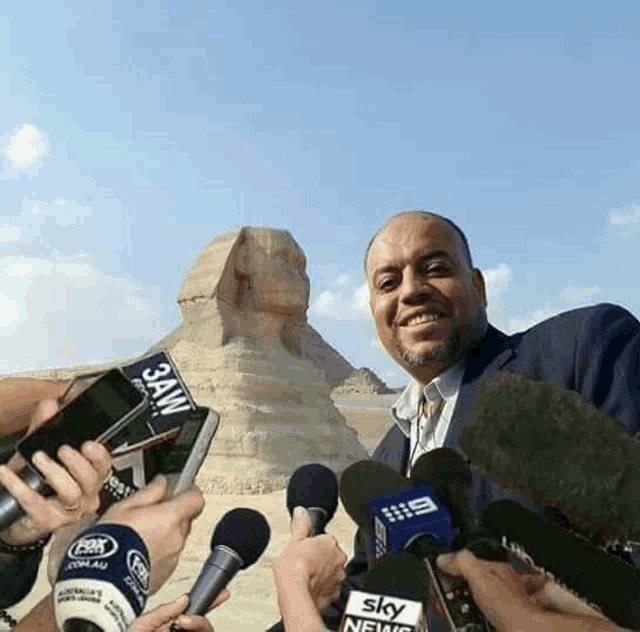 a man is standing in front of a group of microphones with a sign that says sky news