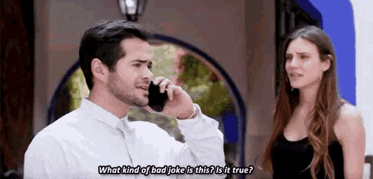 a man is talking on a cell phone while standing next to a woman who is looking at him .