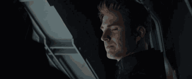 a man with long hair is sitting in a dark room looking down .