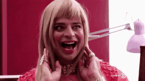 a woman in a wig is making a funny face while being touched by a man in a red dress .
