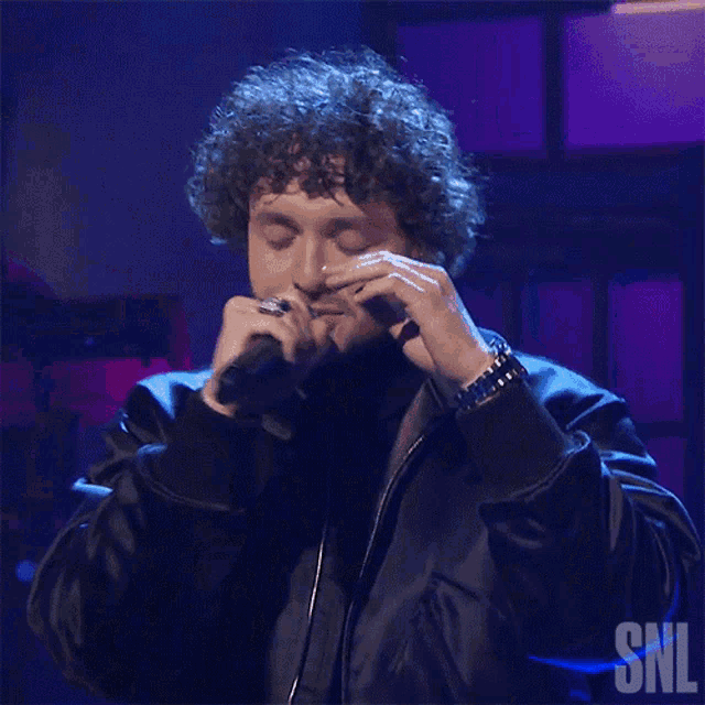 a man singing into a microphone with a snl logo in the corner