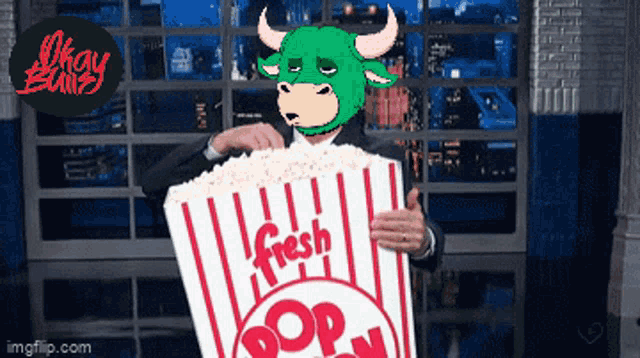 a man wearing a green bull mask is holding a striped bag of fresh popcorn
