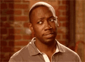 a man in a gray shirt is making a funny face in front of a brick wall .