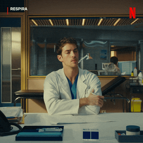 a man in a lab coat sits at a desk with a netflix logo behind him
