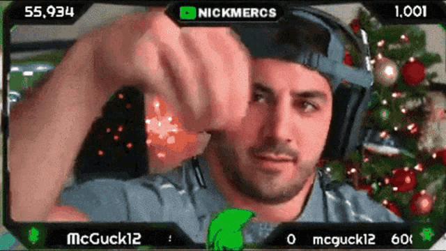 a man wearing headphones is playing a video game with a christmas tree behind him
