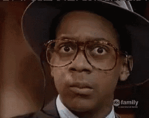a young man wearing glasses and a hat looks at the camera .