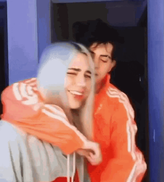a man and a woman are hugging each other in a room . the man is wearing an orange jacket .