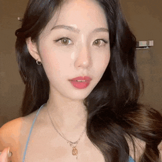 a close up of a woman 's face wearing a blue top and a necklace .