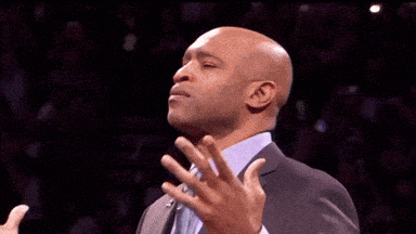 a bald man in a suit and tie is clapping his hands in front of a crowd